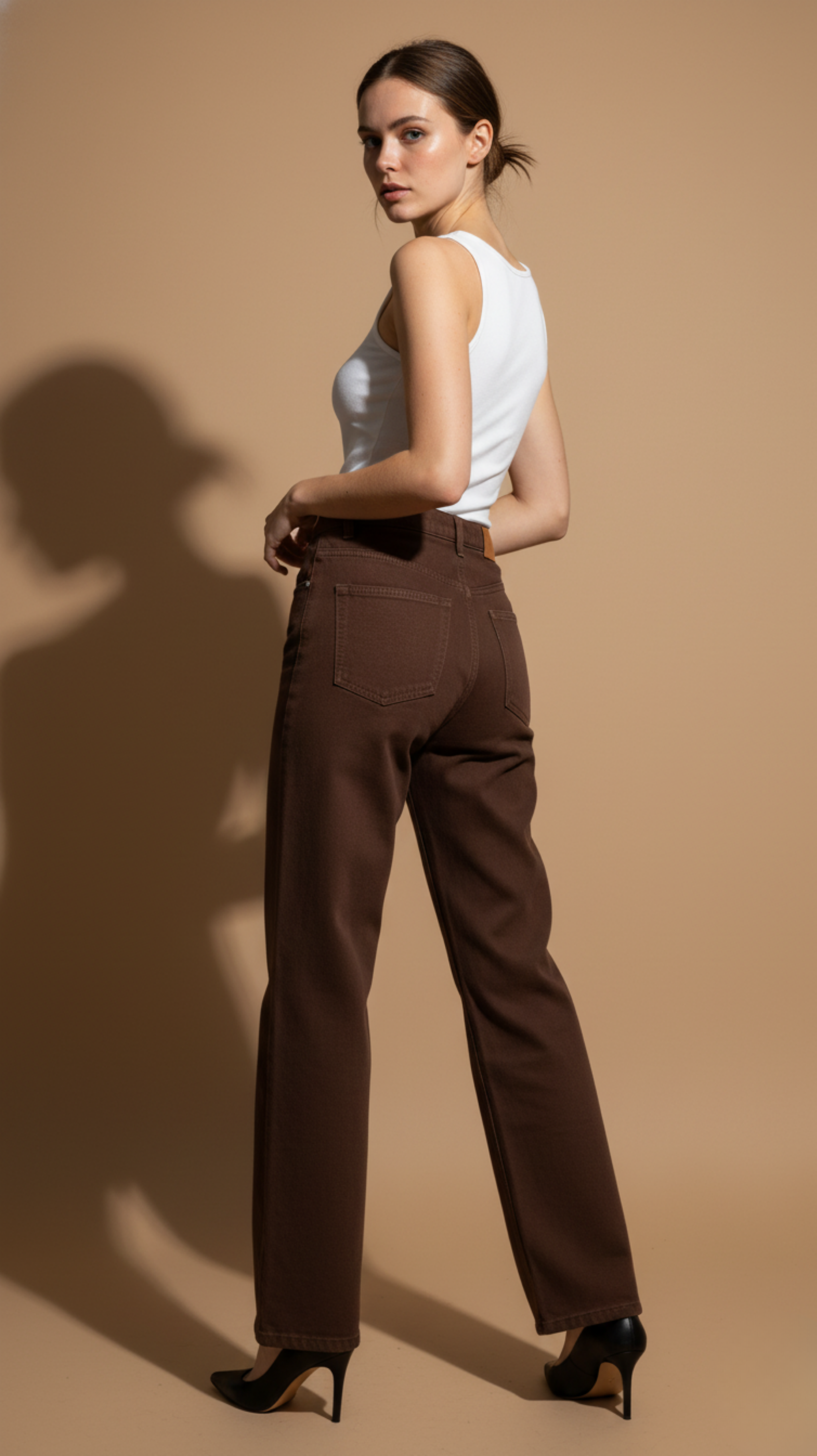 Woman wearing brown pants and a white top against a beige background