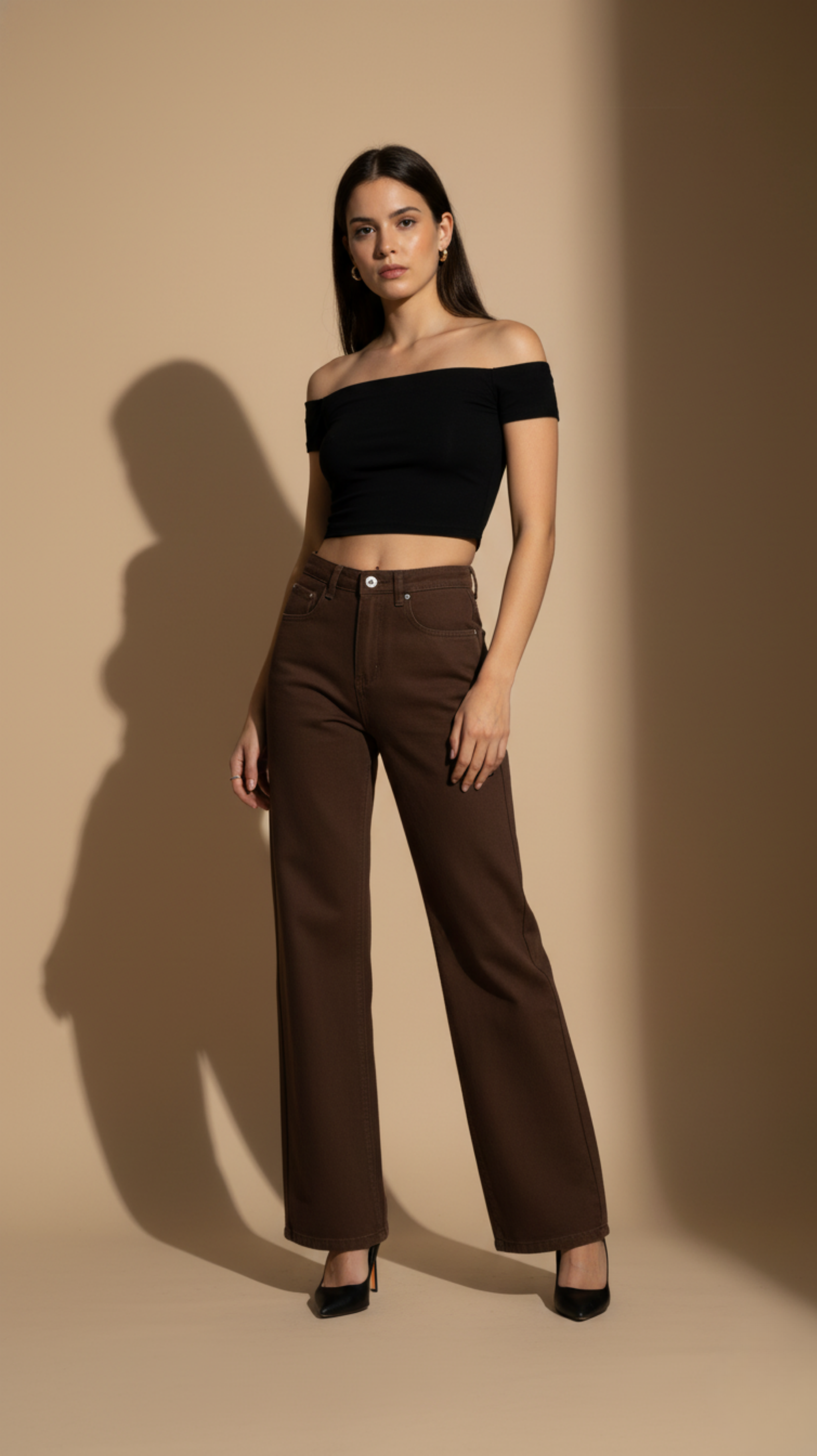 Woman wearing a black off-shoulder top and brown high-waisted pants against a beige background