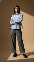 Woman wearing a light blue striped shirt and gray pants against a beige background
