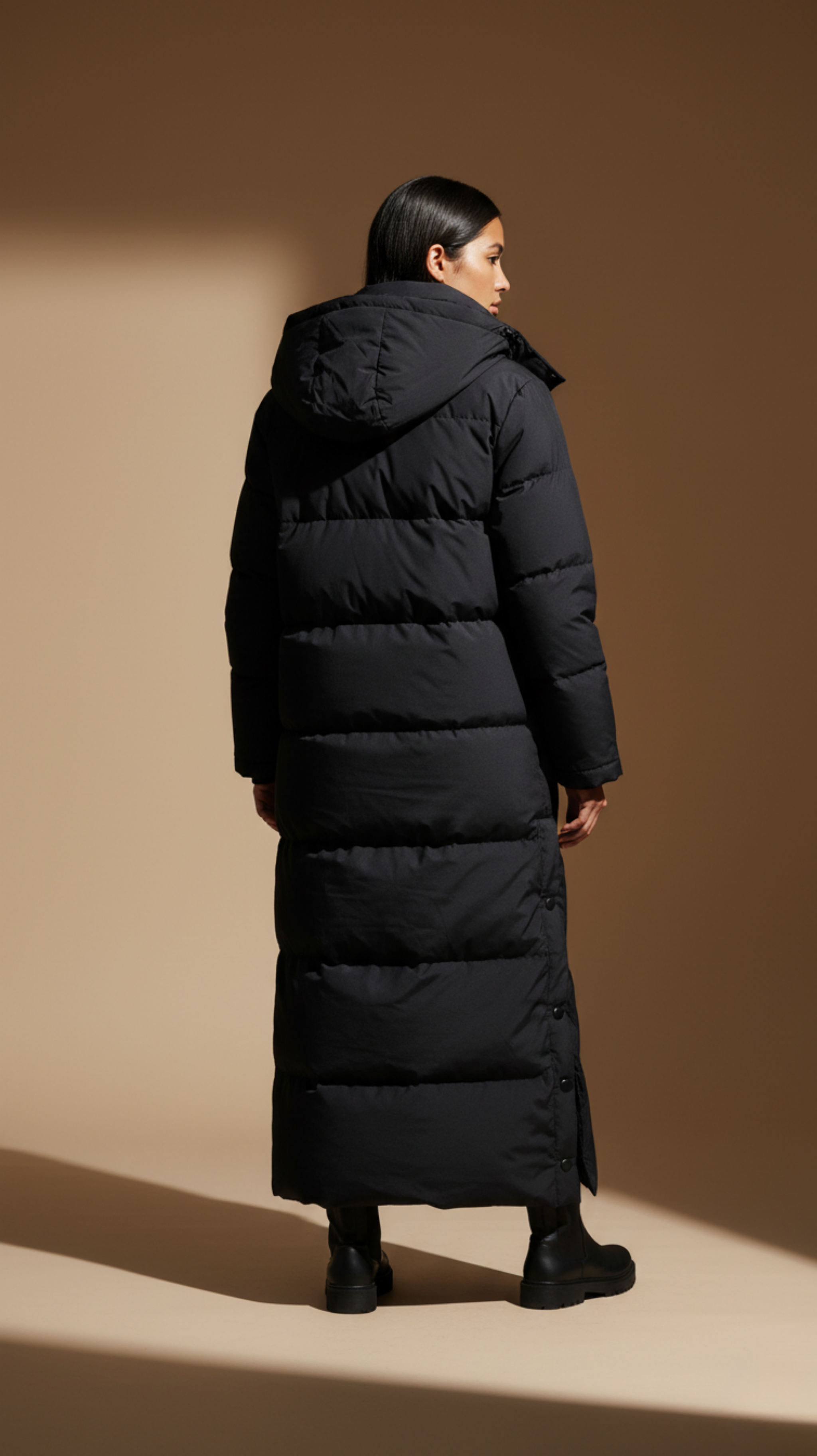 Person wearing a long black puffer coat against a brown background