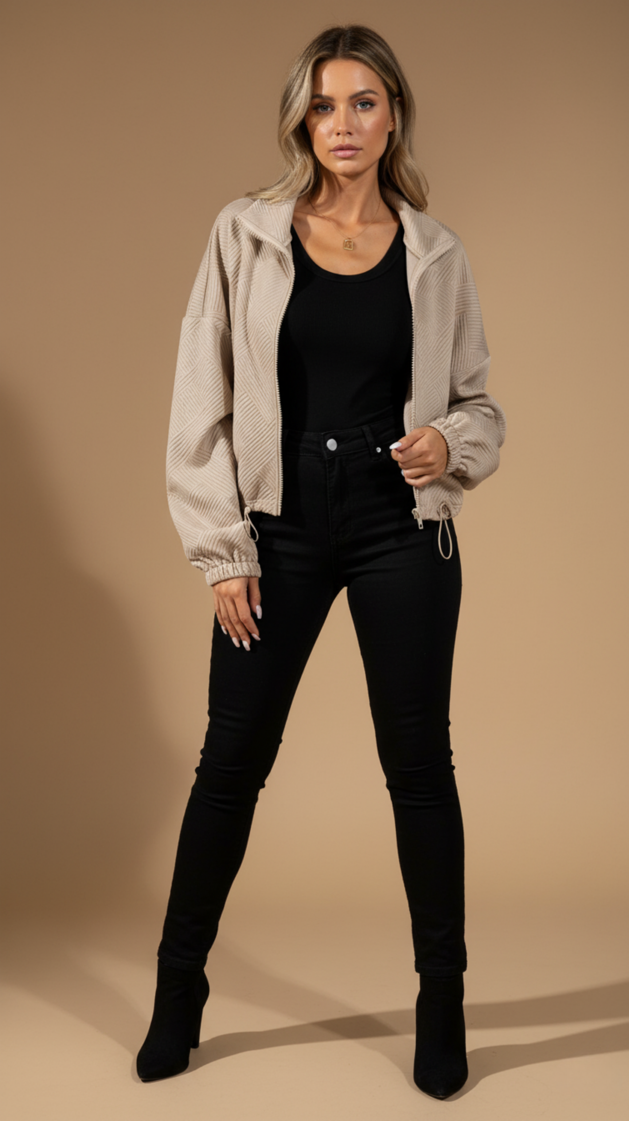 Woman wearing a beige jacket, black top, and black pants on a beige background
