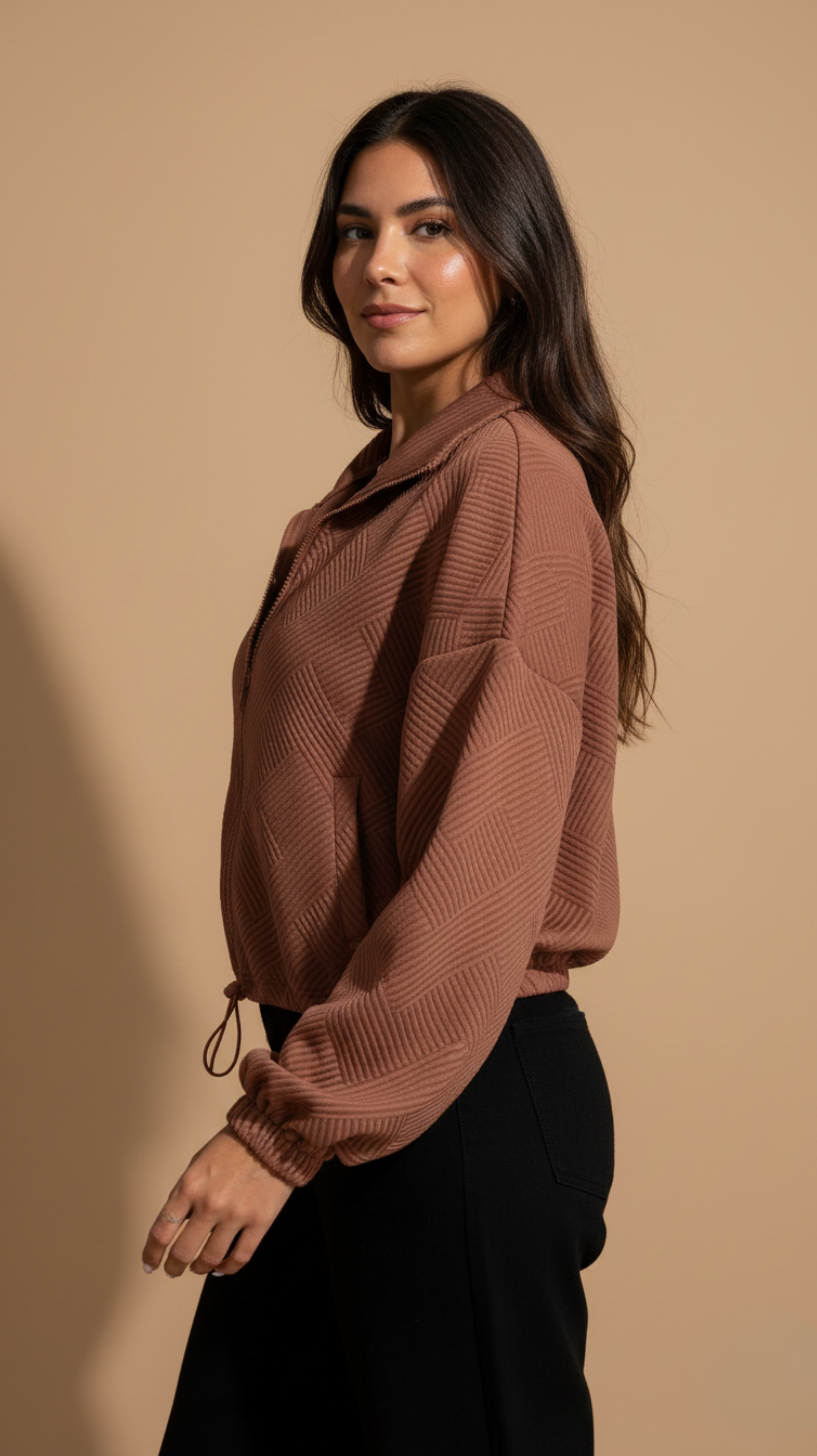 Woman wearing a brown ribbed sweater against a beige background