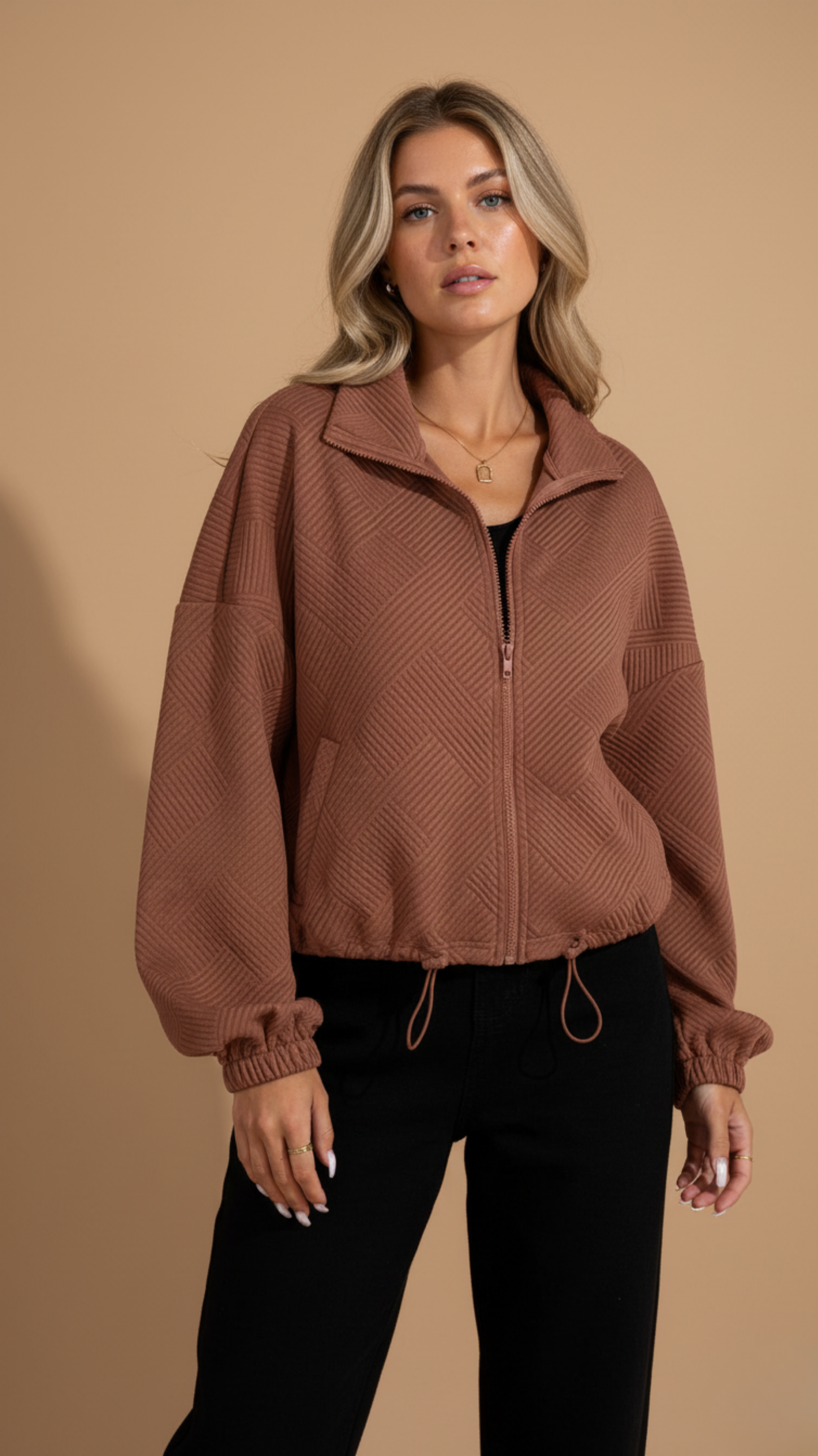 Woman wearing a brown zip-up sweater against a beige background